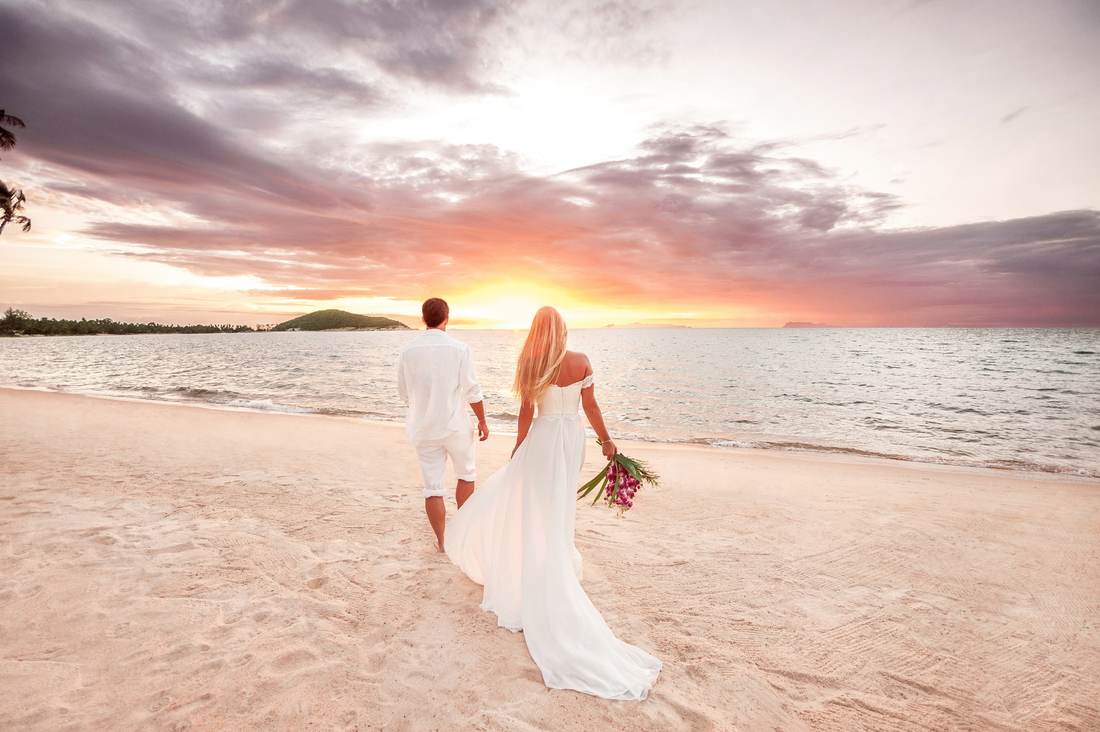 Bride following behind groom on beach